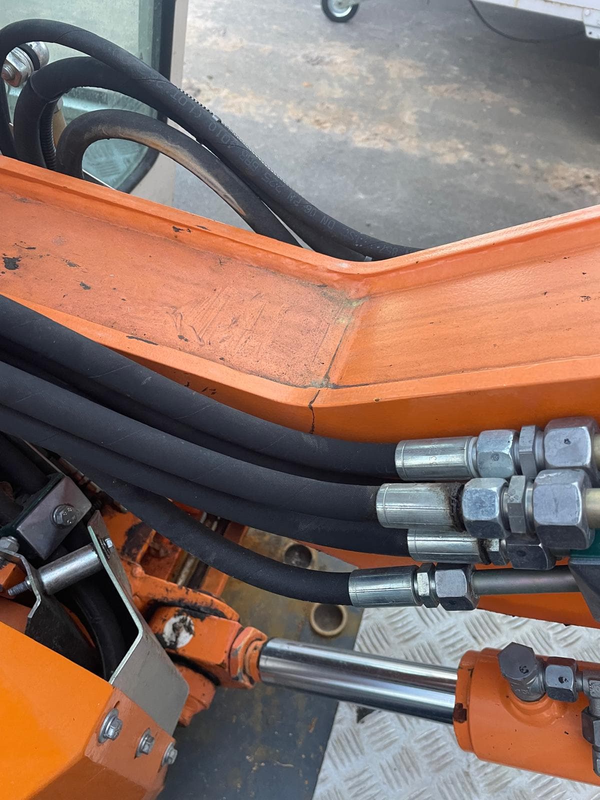 Riss an einem orangefarbenen Maschinenrahmen mit Hydraulikleitungen