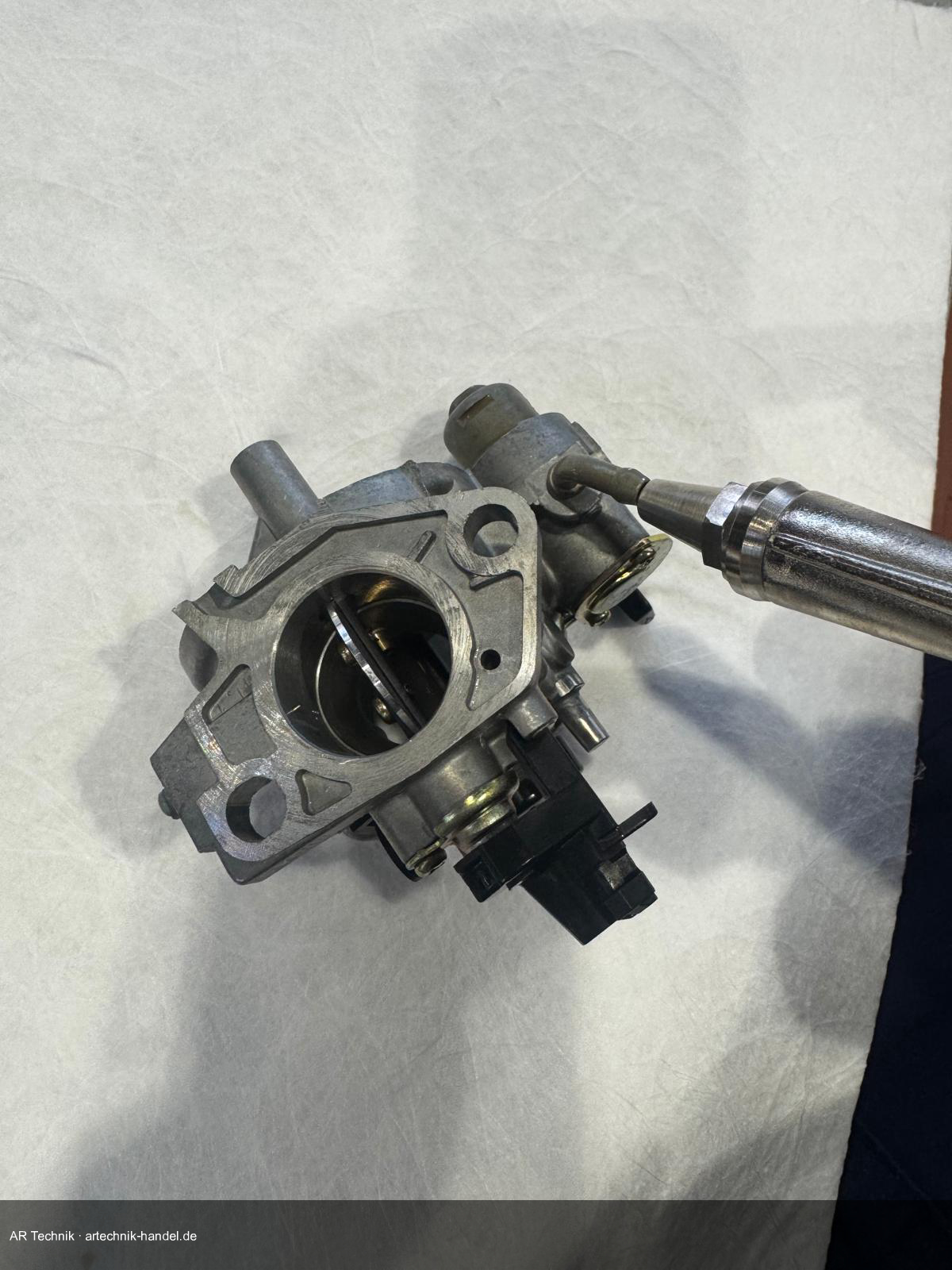 Druckluft durch Düsenbohrungen und Kanäle des Honda GX Vergasers blasen